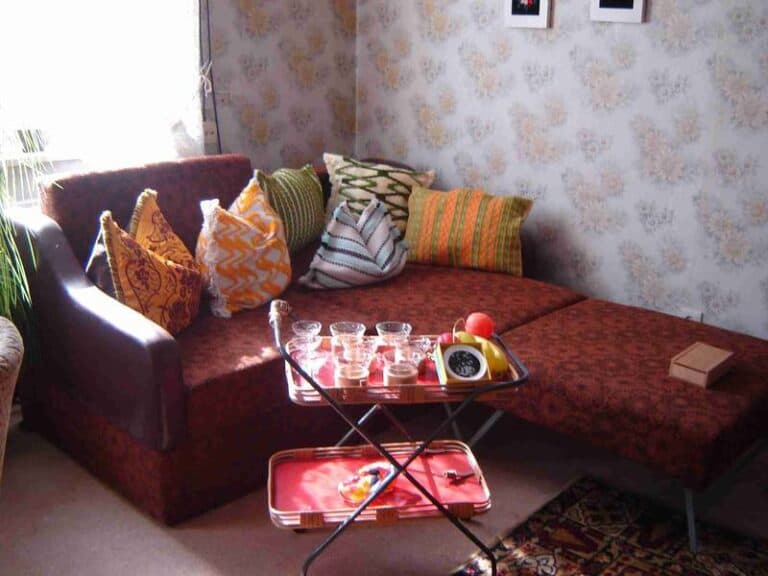 Auf dem Bild ist eine kleine rote Eckcouch mit bunten Kissen zu sehen, vor der ein kleiner Servierwagen steht