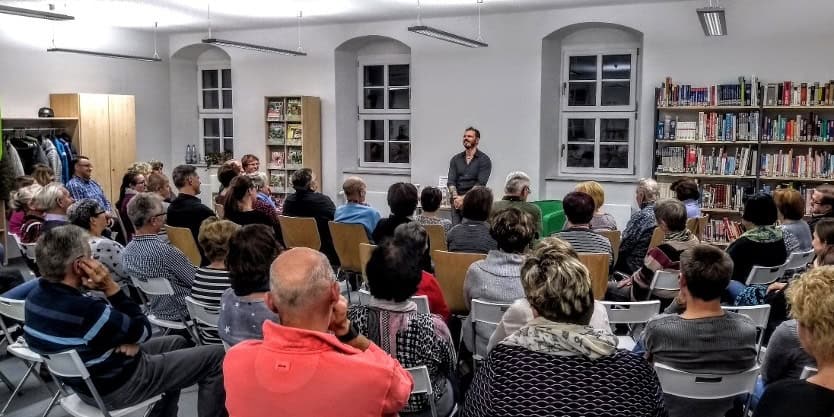 Auf dem Bild ist ein Redner im Meisterhaus zu sehen, der vor einer Gruppe von Menschen spricht