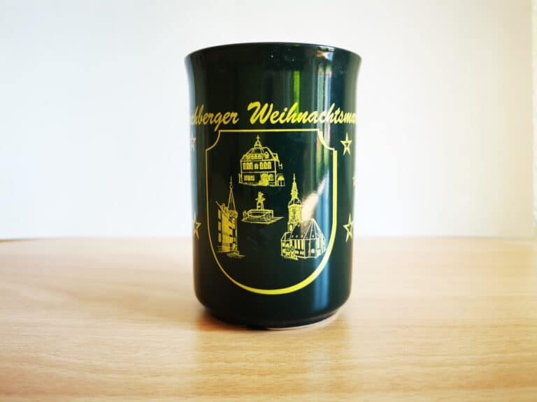 Auf dem Bild ist eine dunkelgrüne Keramiktasse mit Henkel und gelbem Aufdruck vom Kirchberger Weihnachtsmarkt zu sehen
