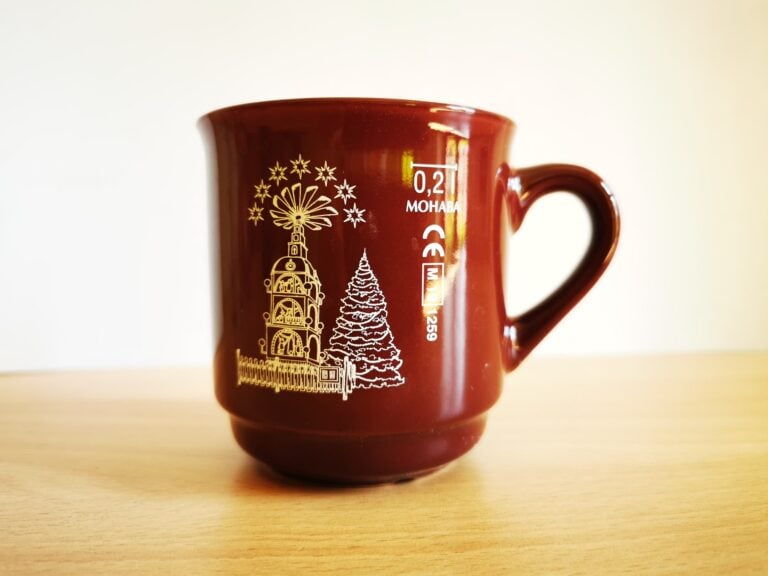 Auf dem Bild ist eine rote Keramiktasse mit Henkel und weißem Weihnachtsmotiv aus Kirchberg zu sehen
