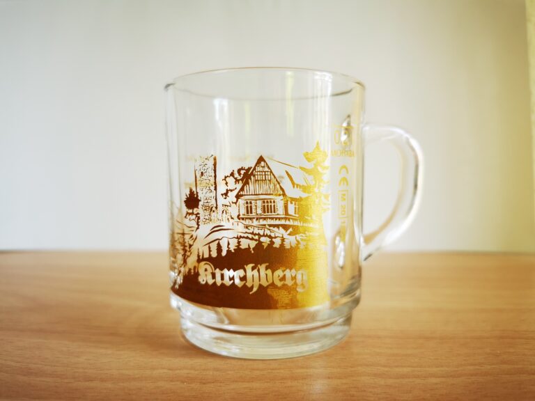 Auf dem Bild ist eine Glastasse mit Henkel und goldenem Weihnachtsmotiv aus Kirchberg zu sehen
