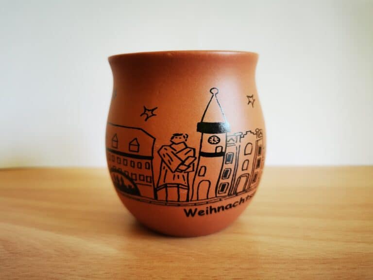 Auf dem Bild ist eine braune Glühweintasse ohne Henkel mit der Silhouette von Kirchberg und dem Schriftzug „Kirchberger Weihnachtsmarkt“ zu sehen