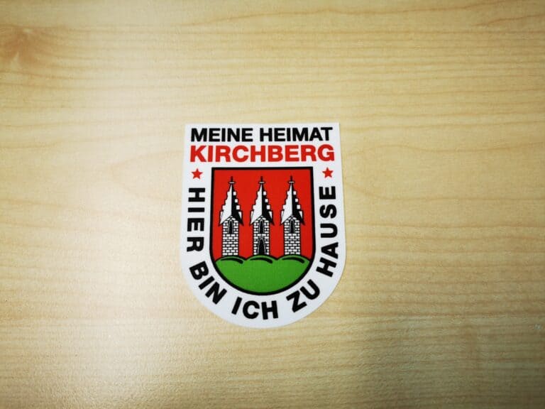 Auf dem Bild ist ein Aufkleber mit dem Schriftzug „MEINE HEIMAT KIRCHBERG – HIER BIN ICH ZU HAUSE“ und dem Wappen der Stadt zu sehen