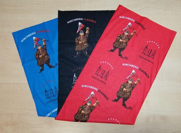 Auf dem Bild sind drei Multifunktionstücher zu sehen. Sie sind in Blau, Schwarz und Rot gestaltet und zeigen das Kirchberg-Logo, das Maskottchen Schraubermichl und den Schriftzug „Kirchberg Classics“