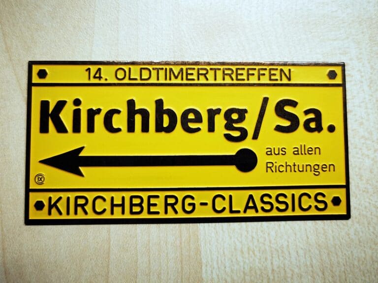Auf dem Bild ist eine messinggelbe Plakette „Kirchberg Classics“ mit mehreren Schriftzügen, darunter „14. Oldtimertreffen“ und „aus allen Richtungen“, zu sehen