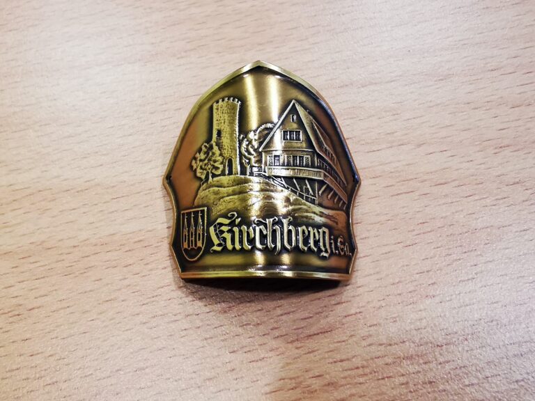 Auf dem Bild ist ein goldener Stocknagel mit der Aufschrift "Kirchberg i. Sa.", sowie einer kleinen landschaftlichen Illustration zu sehen