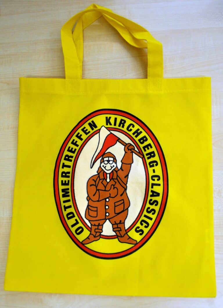 Auf dem Bild sind eine gelbe Tragetasche mit einer Illustration des Schrauber Michls und einer Aufschrift "Oldtimertreffen Kirchberg - Classics" zu sehen