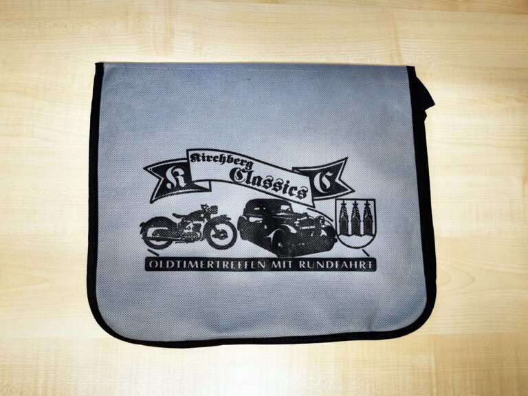 Auf dem Bild ist eine graue Umhängetasche mit dem Aufdruck „Kirchberg Classics – Oldtimertreffen mit Rundfahrt“ und mehreren Oldtimer-Illustrationen zu sehen.