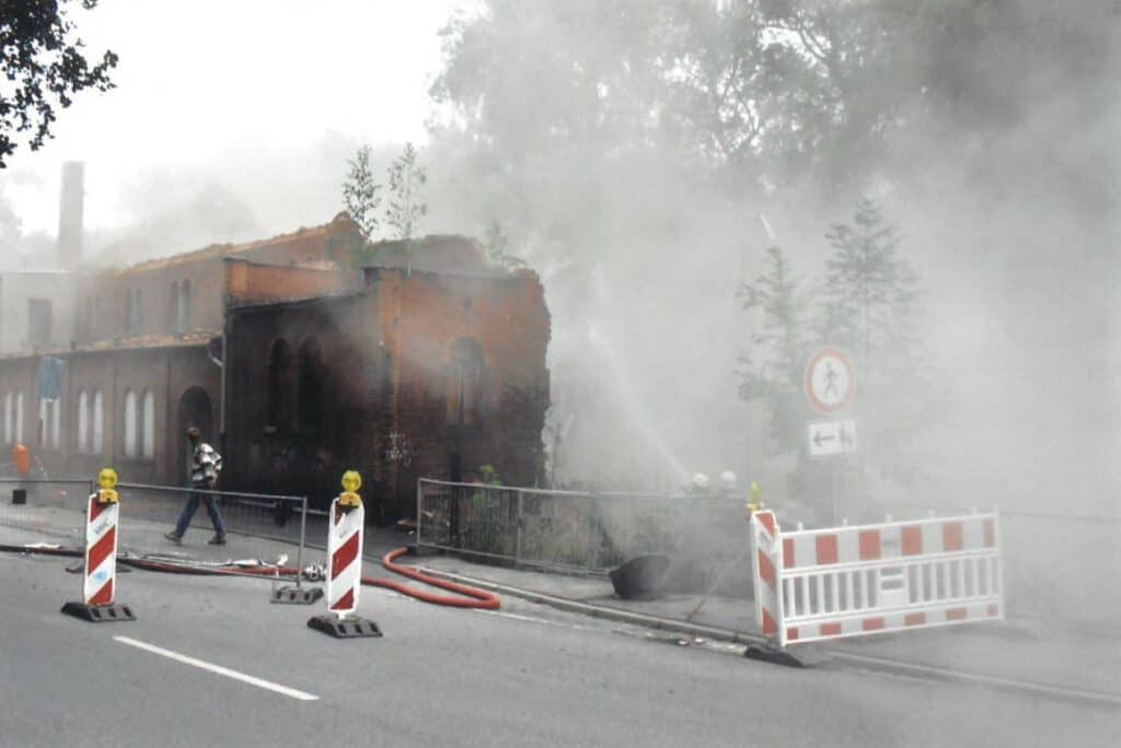 Auf dem Bild sind Feuerwehrleute zu sehen, die einen Löschschlauch auf das eingerissene Gebäude richten