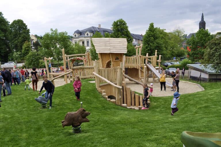 Auf dem Bild ist ein Spielplatz mit vielen Kindern und Erwachsenen zu sehen