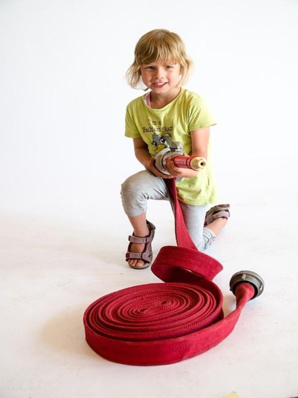 Auf dem Bild ist ein kleines Kind mit einem Feuerwehrschlauch in der Hand zu sehen