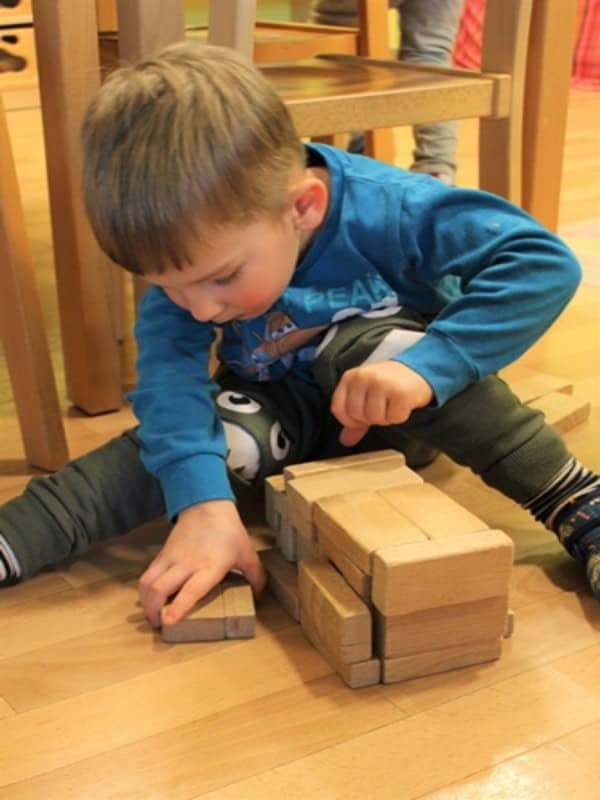 Auf dem Bild ist ein kleiner Junge zu sehen, der mit Bauklötzen spielt