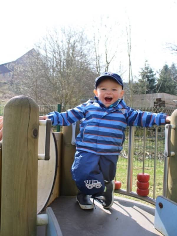 Auf dem Bild ist ein kleiner Junge zu sehen, der auf einem Klettergerüst steht