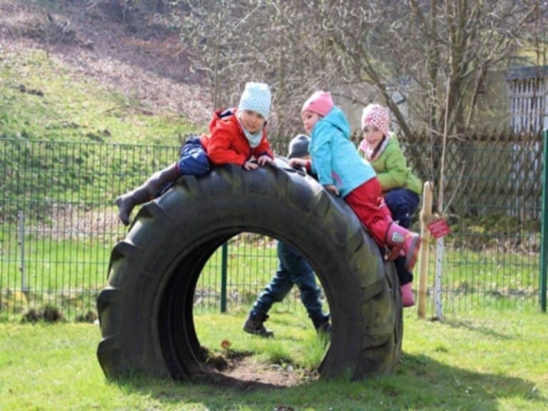 Auf dem Bild sind Kinder zu sehen, die im Freien auf einem Reifen klettern