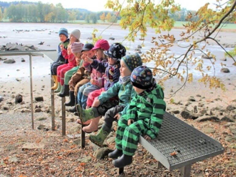 Auf dem Bild ist eine Gruppe Kinder zu sehen, die vor einem See sitzt