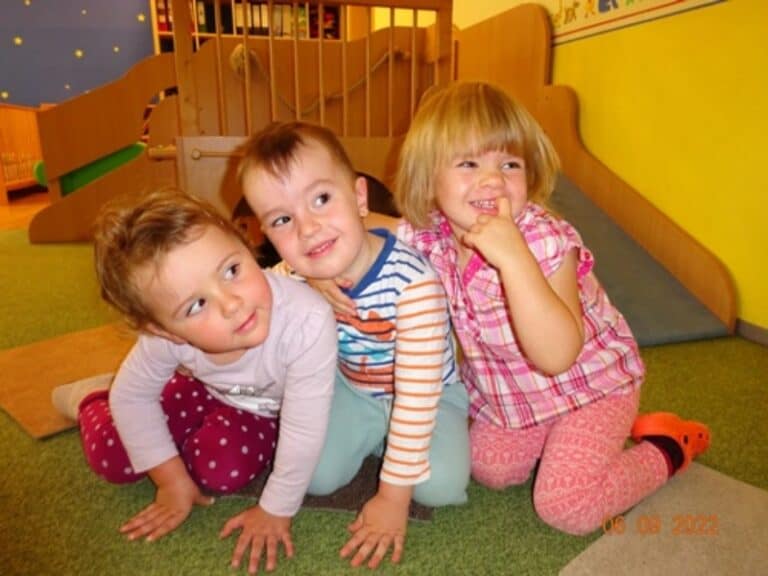 Auf dem Bild sind drei Kinder zu sehen, die zusammen auf dem Boden sitzen