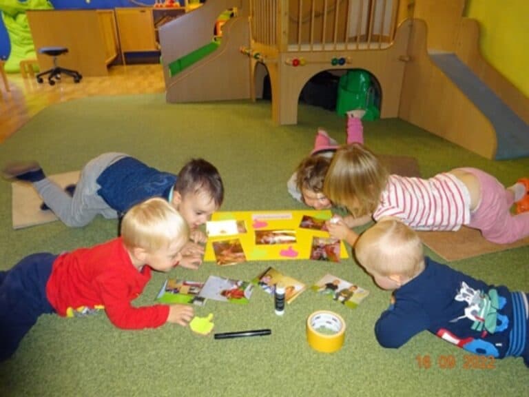 Auf dem Bild sind Kinder zu sehen, die auf dem Boden liegen und gemeinsam basteln