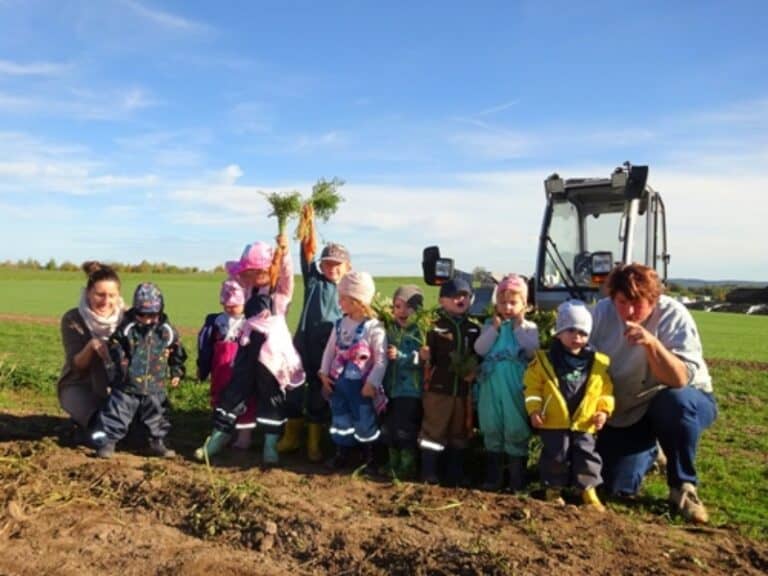 Auf dem Bild ist eine Gruppe Kinder zu sehen, die auf einem Feld vor einem kleinen Radlader steht