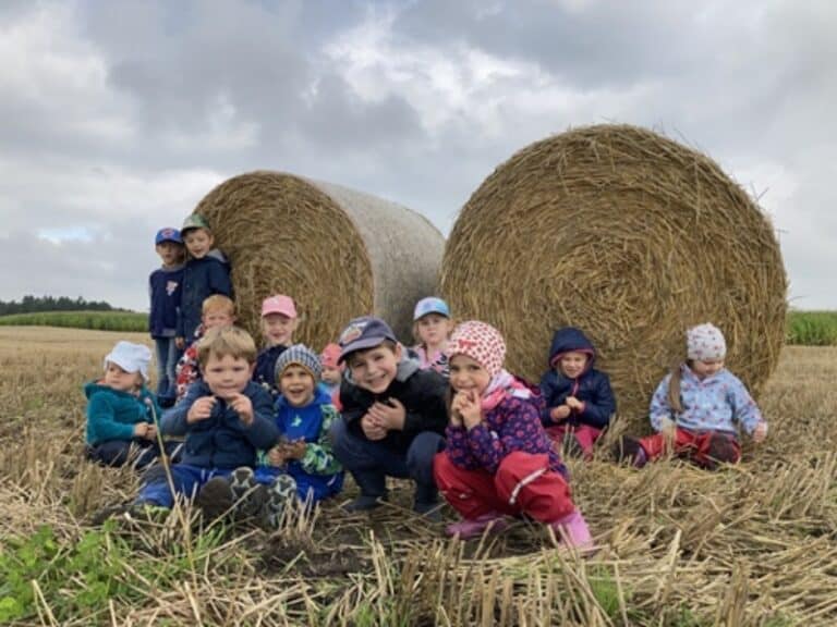 Auf dem Bild sitzt eine Gruppe Kinder vor zwei Strohballen