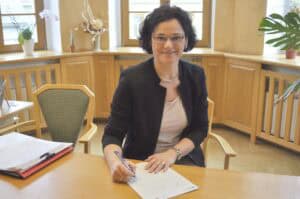 Auf dem Bild ist die Bürgermeisterin Dorothee Obst zu sehen, die an einem Tisch sitzt und etwas auf ein Blatt Papier schreibt