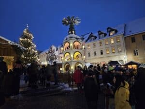 Auf dem Bild ist zu sehen wie viele Menschen am Abend auf dem Kirchberger Weihnachtsmarkt stehen